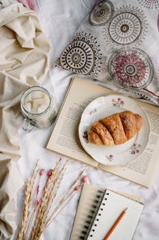 A cozy flat lay of a croissant, book, and iced drink, perfect for a relaxing morning.
