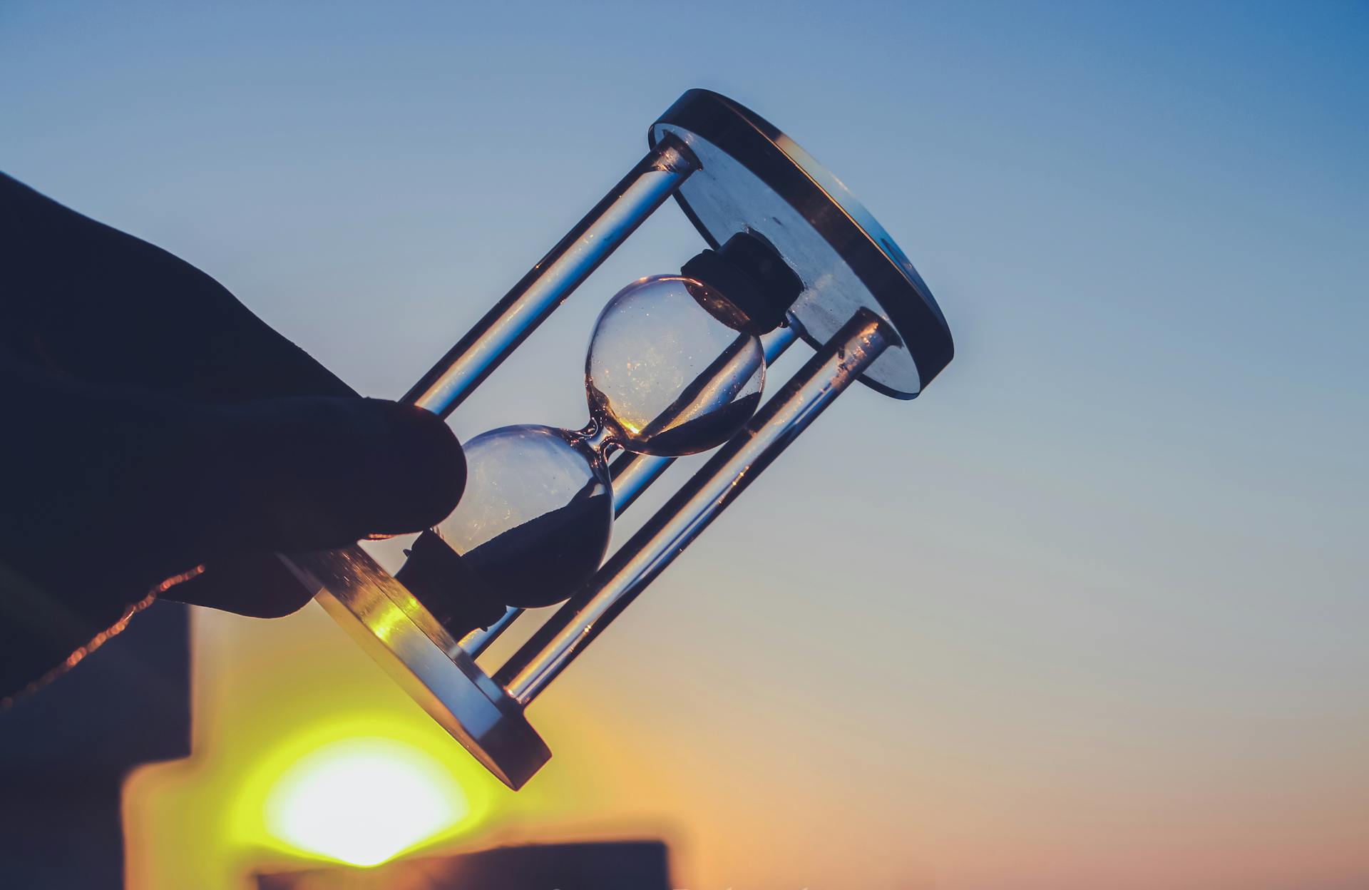 Silhouette of an hourglass held against a vibrant sunset sky in Syria. Time concept.