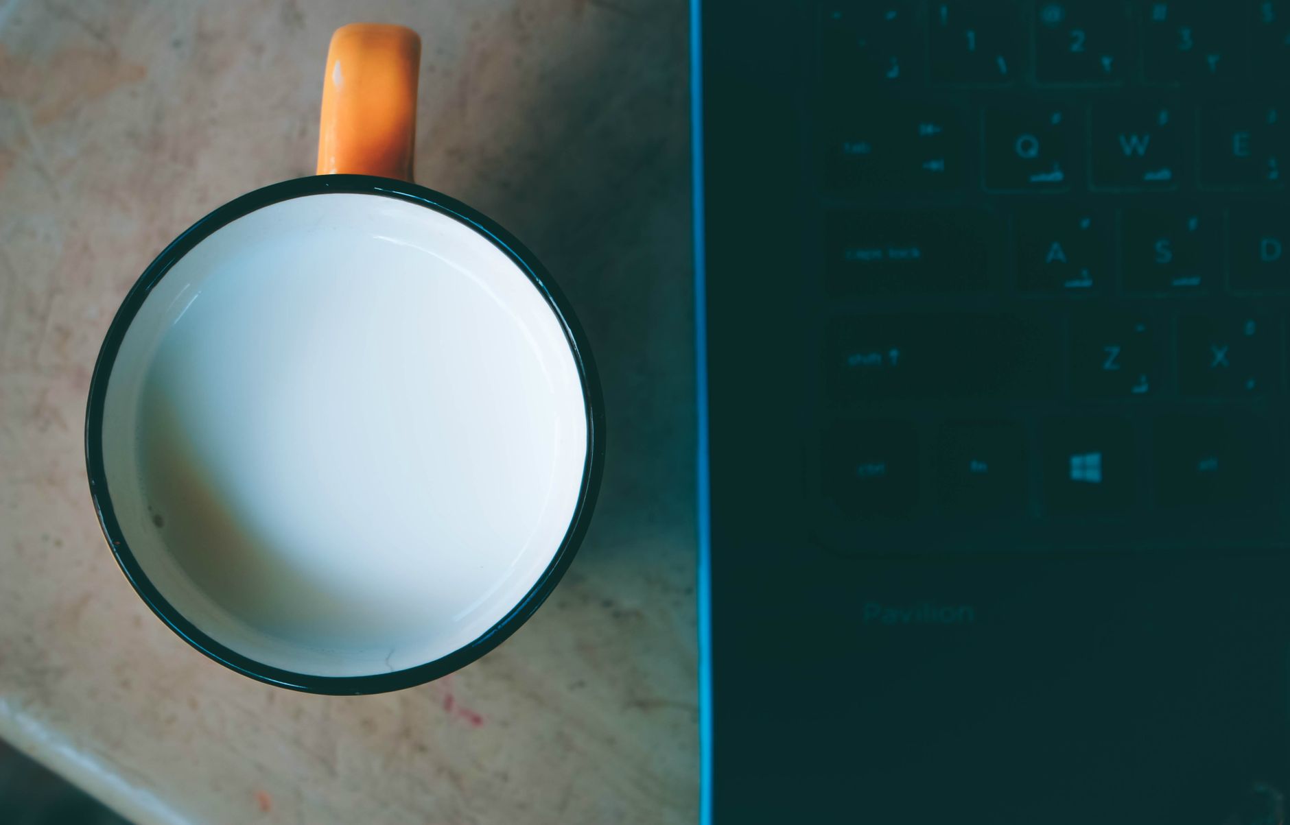 A top-down view of a coffee mug beside a laptop keyboard on a desk indoors.