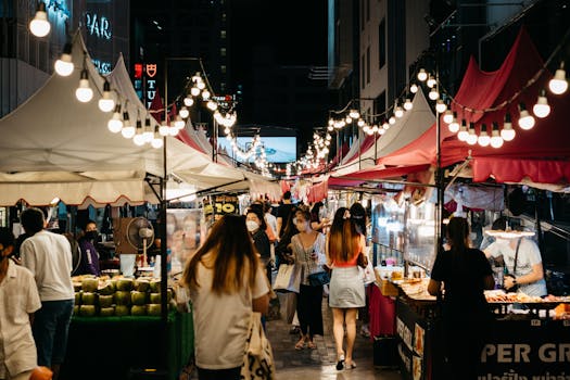 Bustling night market scene with shoppers exploring colorful stalls and string lights.