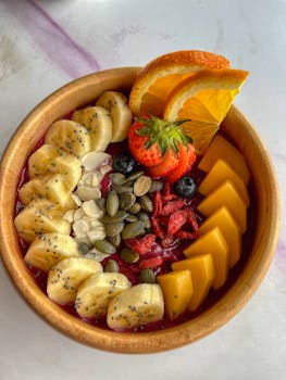Colorful smoothie bowl with banana, mango, nuts, seeds, and fresh fruits in a wooden bowl.