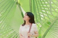 一位快乐的年轻女子在户外享受着阳光明媚的一天，微笑着欣赏郁郁葱葱的热带棕榈叶