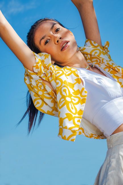 Stylish young woman posing confidently under a bright blue sky, showcasing trendy fashion.