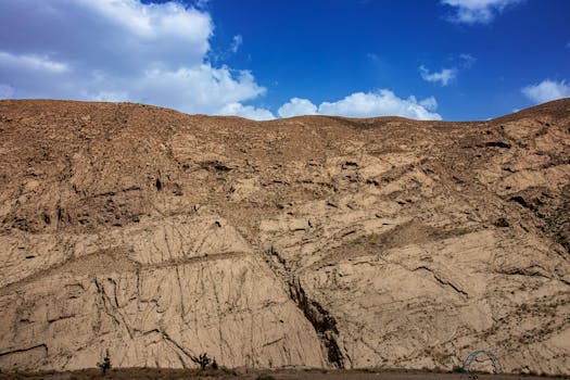 Explore the rugged beauty of a rocky mountainside with clear blue skies and white clouds above.