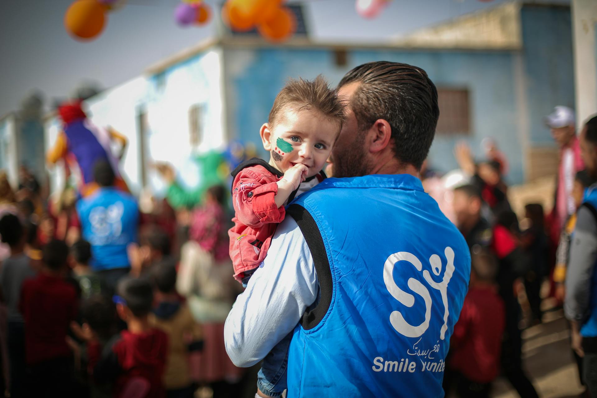 A volunteer holds a toddler during a charity event in Idlib, Syria, symbolizing hope and community.