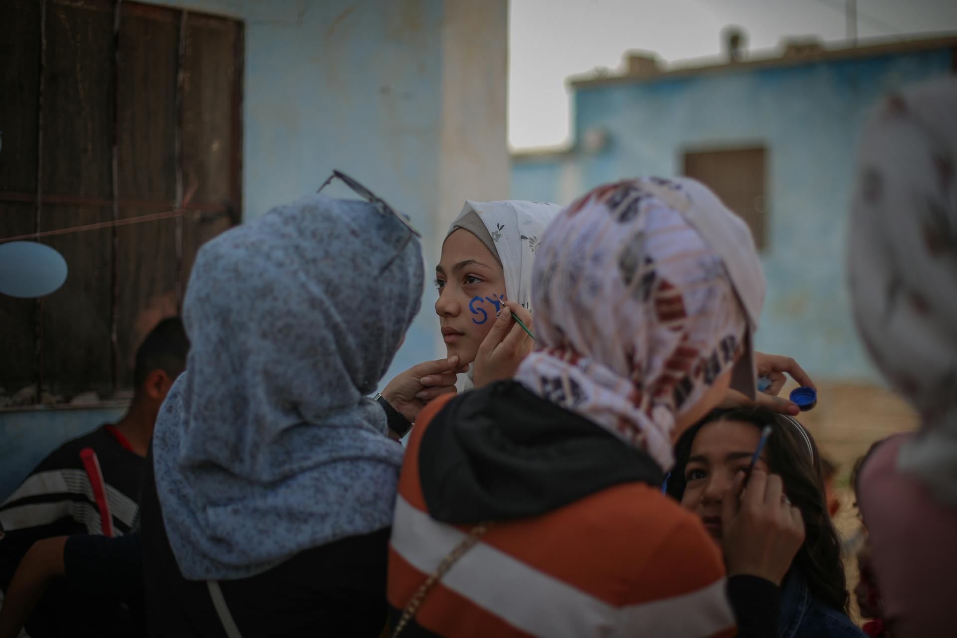 Group of young girls in hijabs applying face paint outdoors in Idlib, Syria, showcasing cultural unity.