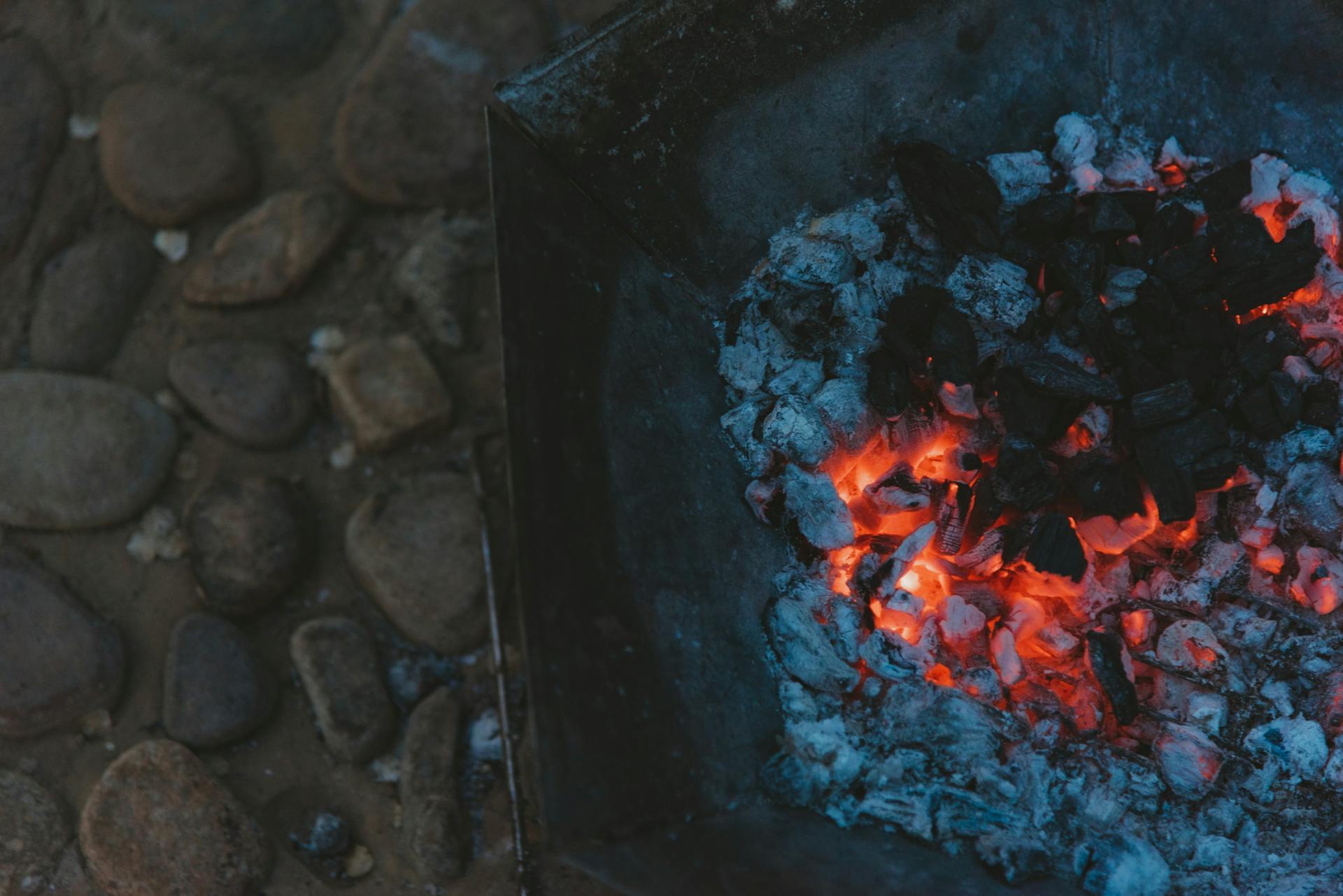 Detailed shot of burning charcoal and embers in a metal container with rocky background.