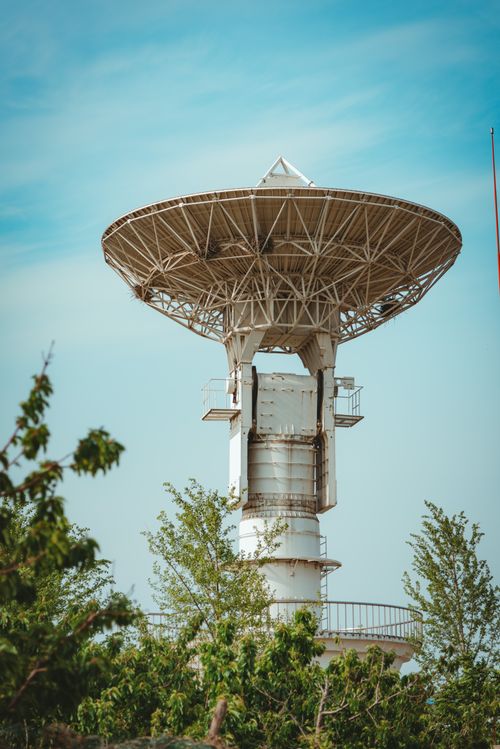 Free A modern satellite broadcast tower amidst trees under a clear blue sky. Stock Photo