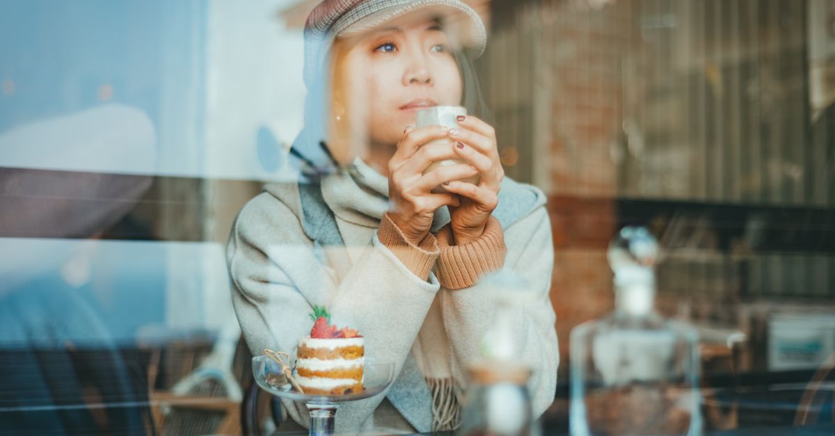 person looking out a window at a city street, deep in thought, holding a coffee cup