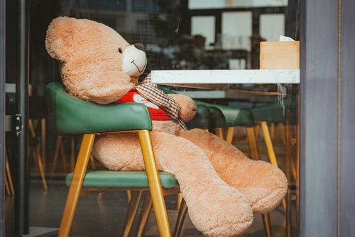 Free Cute plush teddy bear sitting in a chair inside a cafe. Cozy and charming indoor scene. Stock Photo