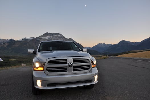 Silver pickup truck parked on mountain road at sunset with scenic view.