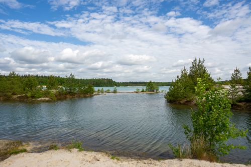 Free Peaceful lake surrounded by trees under a clear blue sky with white clouds. Stock Photo