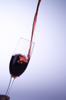 Dramatic capture of red wine flowing into a glass against a plain background.