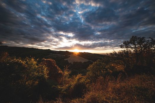 Vibrant sunset casting dramatic light over lush landscape and cloudy sky.
