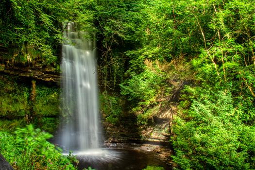 Stunning long exposure of a waterfall surrounded by vibrant greenery in a serene Irish forest.