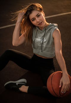 Confident young woman in hoodie holding a basketball on outdoor court