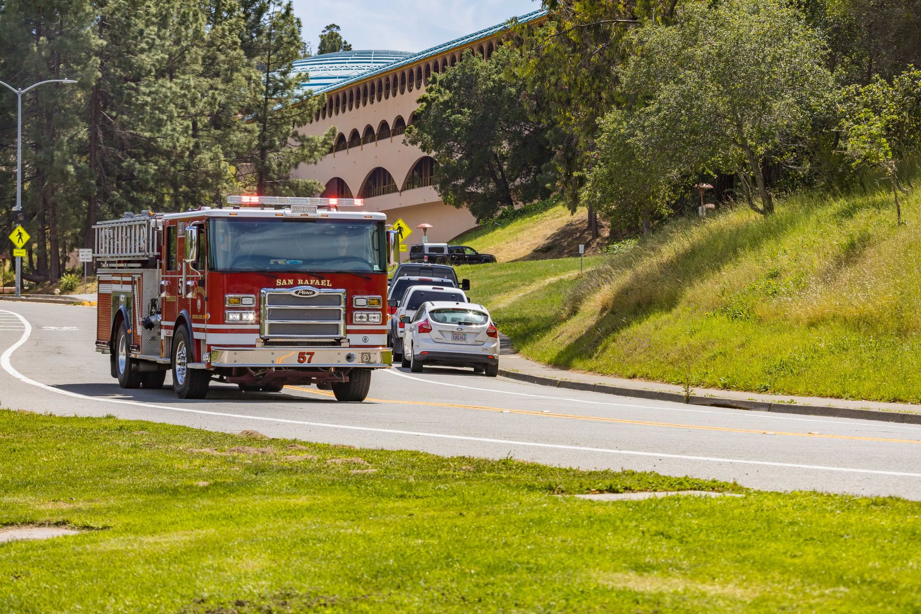 Red fire truck on a curvy road surrounded by lush greenery near a San Rafael landmark.