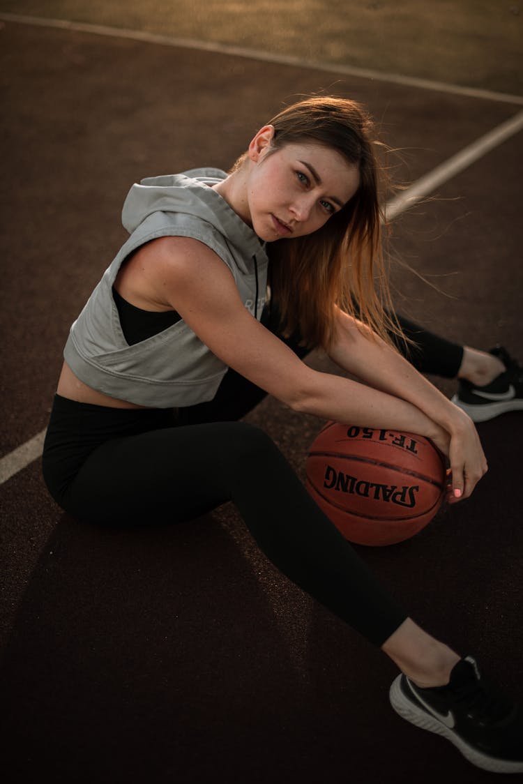 Woman Sitting On Court Holding Basketball