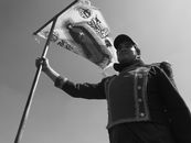 Black and white portrait of a man holding a religious banner outdoors.