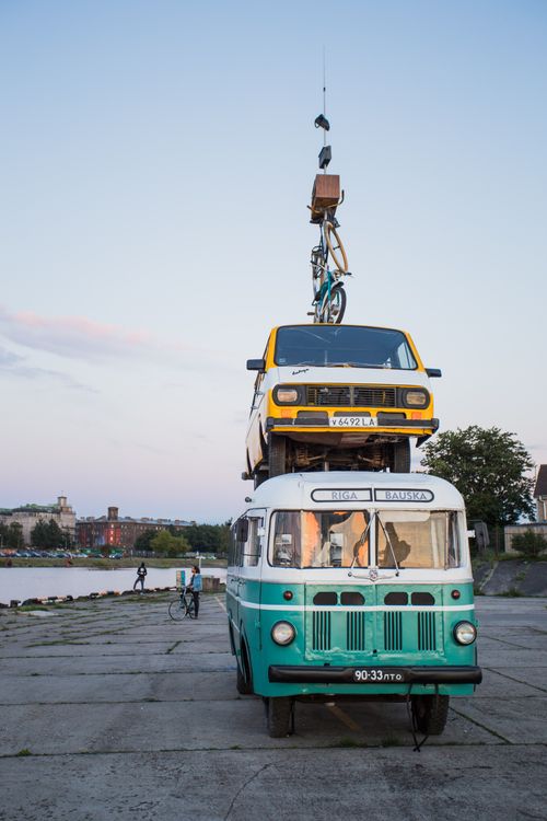 Free Creative stacking of vehicles including a bus, car, and bicycle near the riverbank. Stock Photo