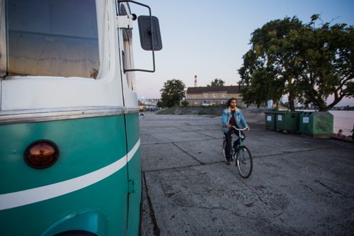 Free A cyclist rides past a vintage bus in a cityscape during sunset, creating a serene urban mood. Stock Photo