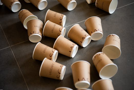 Multiple branded disposable paper cups scattered on a tile floor, symbolizing waste.