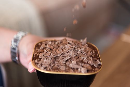 Free A person prepares a delicious chocolate dessert in a bowl with grated chocolate on top. Stock Photo