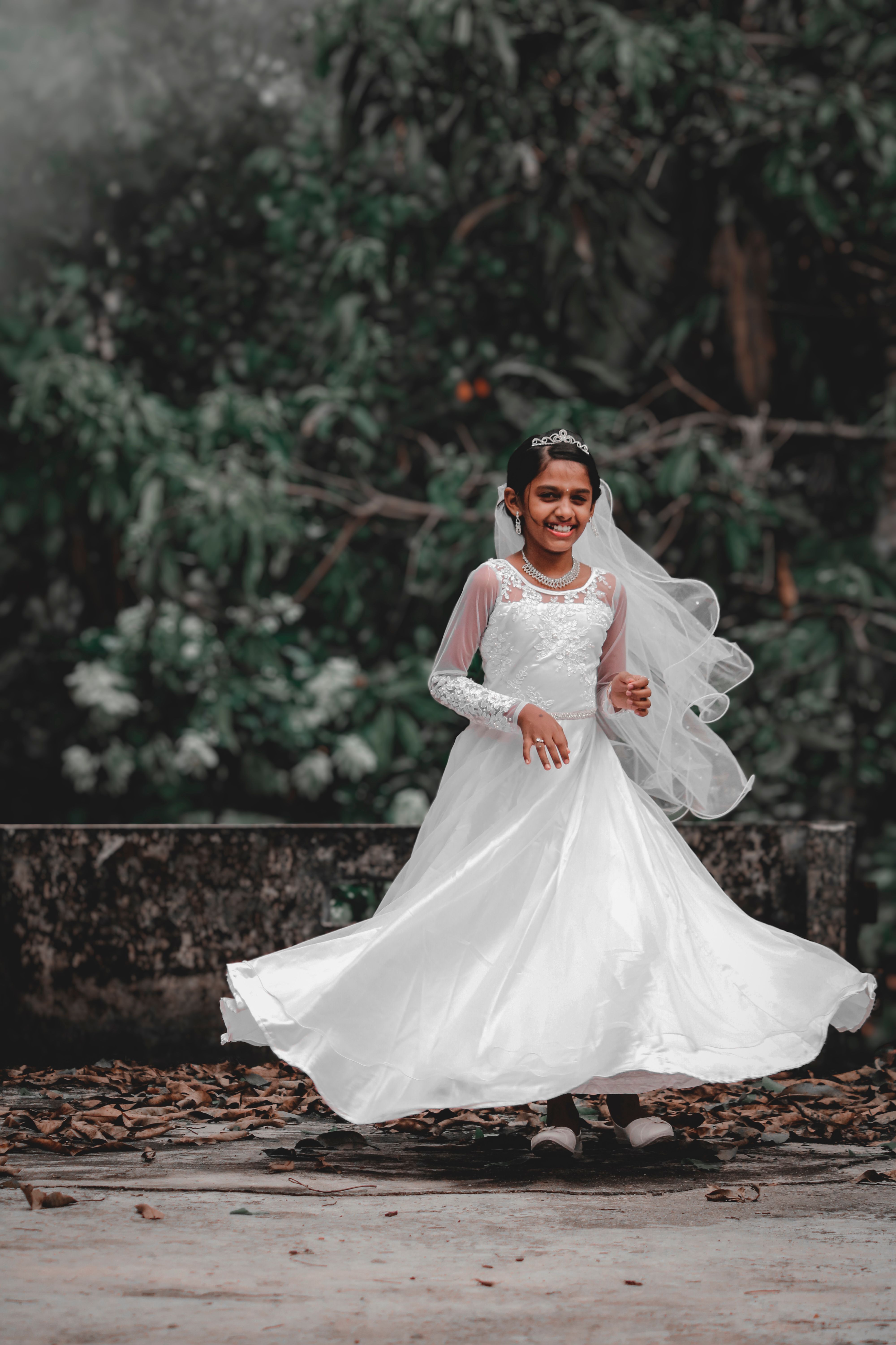 A happy girl twirls in her white gown outdoors, exuding joy and innocence.