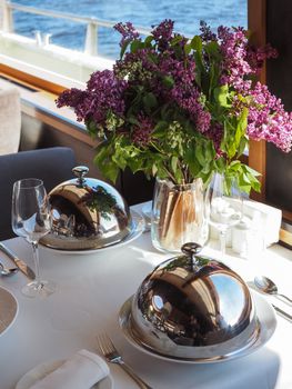 Elegant dining setup with a bouquet of lilacs in a vase and covered dishes.
