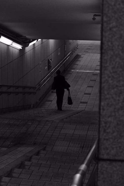 Black and White Photo of a Person Walking into a Tunnel