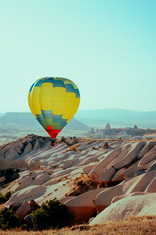 Free Bright hot air balloon soaring over Cappadocia's unique rocky landscape under clear skies. Stock Photo