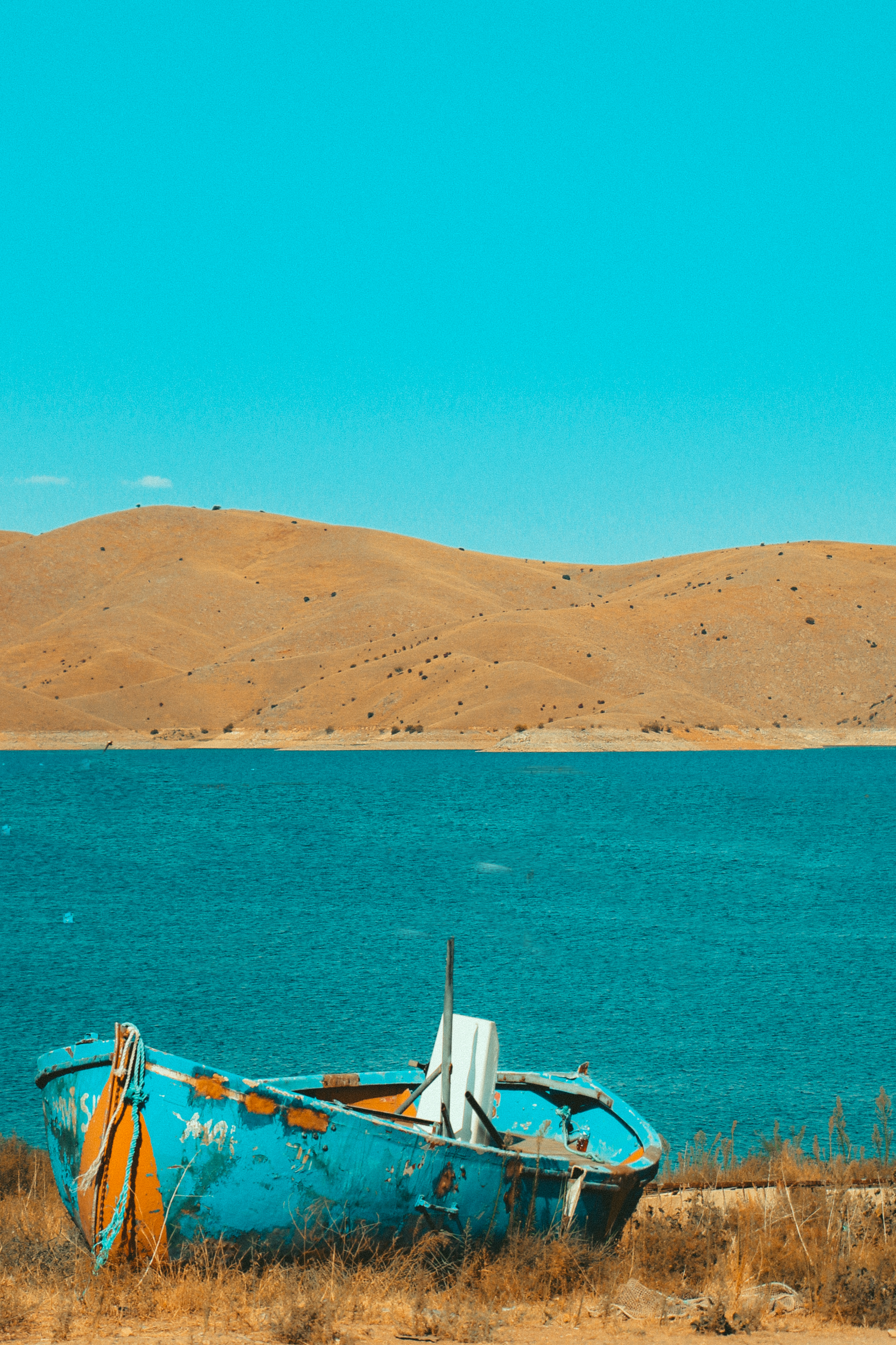 A vintage wooden boat on dry land with turquoise waters and hills in the background.