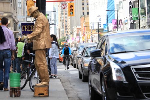 Free A bustling urban scene in Toronto featuring cars, a cyclist, and a street performer. Stock Photo