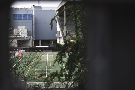 View of a sports field adjacent to a modern stadium, framed by greenery.