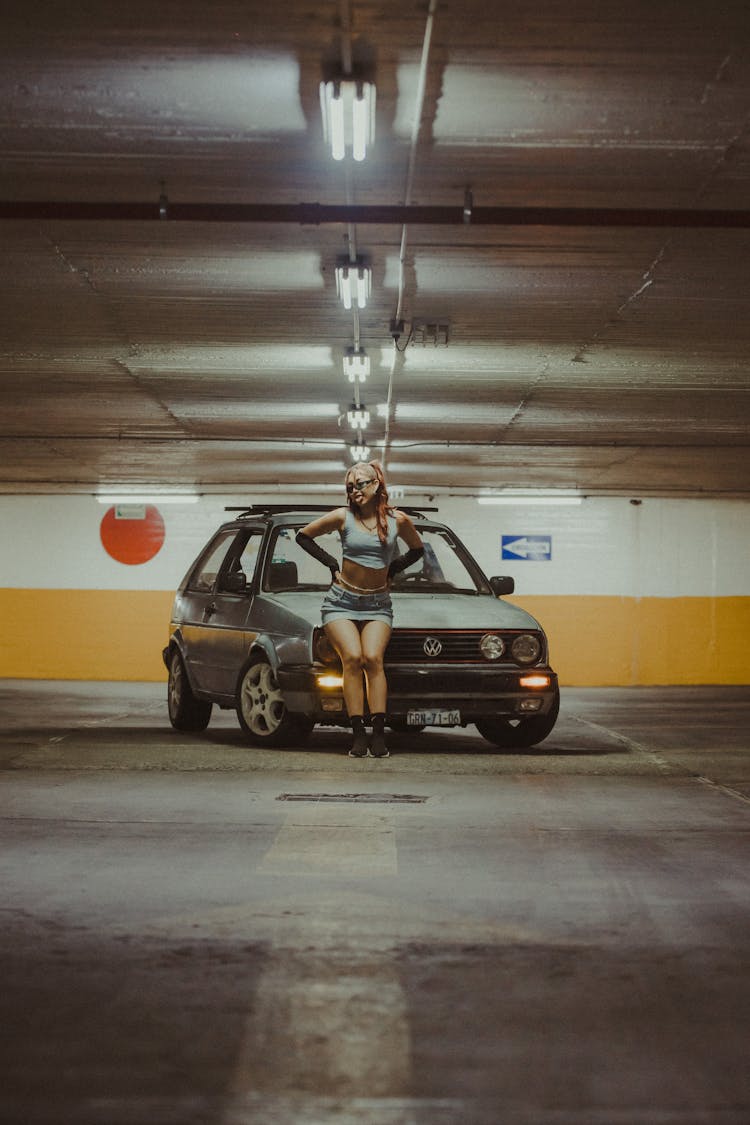  A Woman In Blue Tank Top And Denim Skirt Sitting On A Car Hood