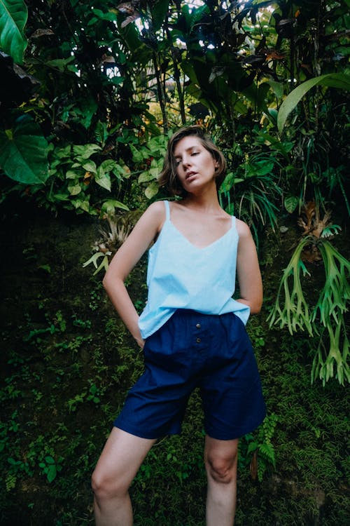 Woman in White Spaghetti Strap Top and Blue Shorts Standing Beside Green Plants