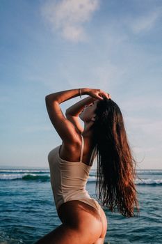 Woman in swimsuit posing by ocean with long hair, under clear sky. Summer vibes.