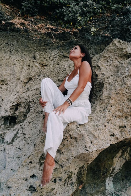 Barefoot Woman in White Suit Sitting on Rocks