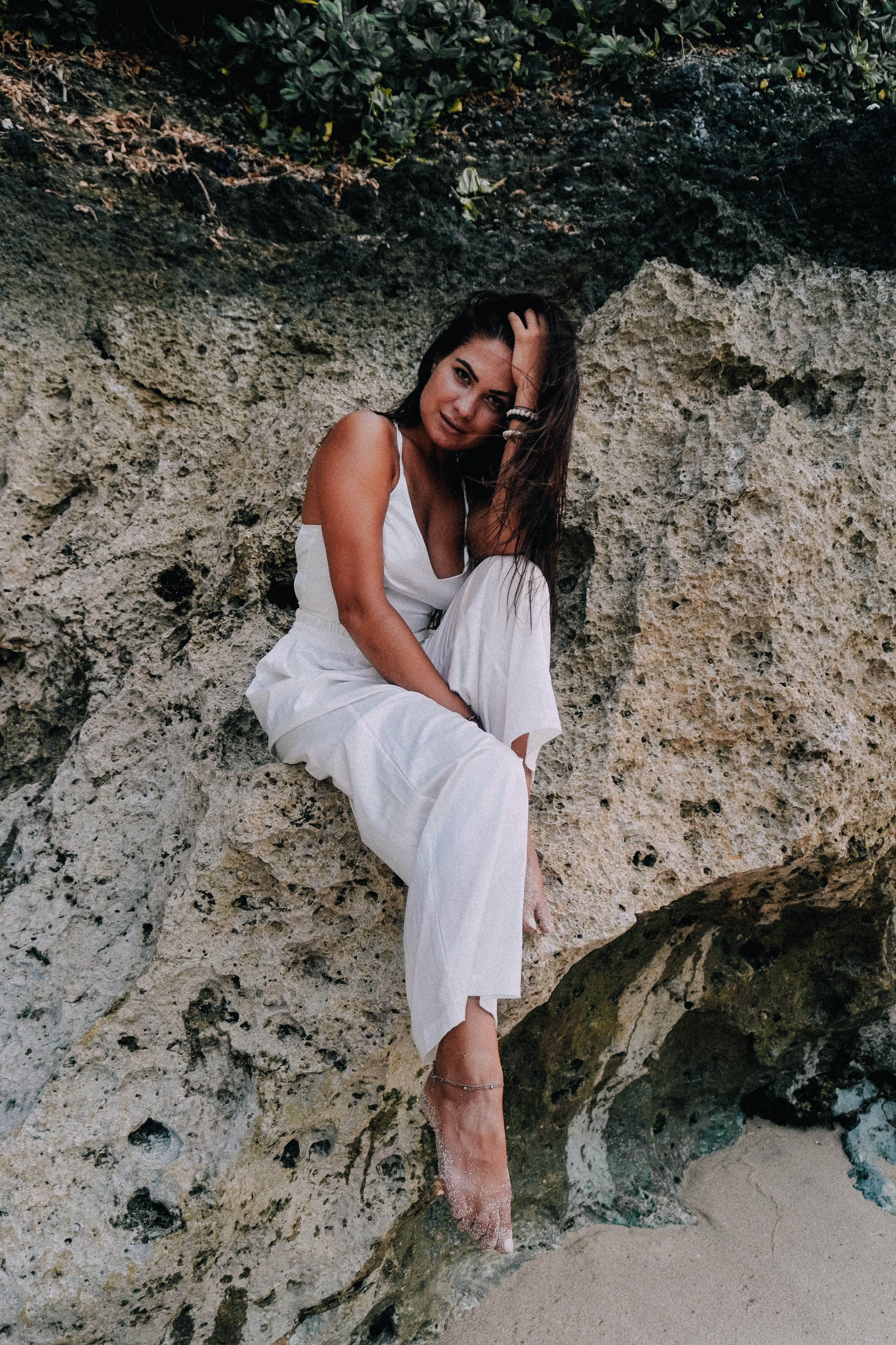 Woman in White Suit Sitting at Base of Rocky Cliff · Free Stock Photo