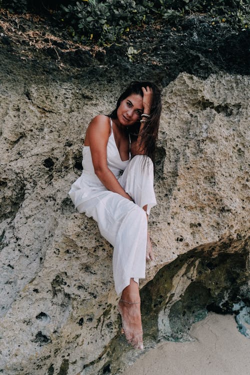 Woman in White Suit Sitting at Base of Rocky Cliff