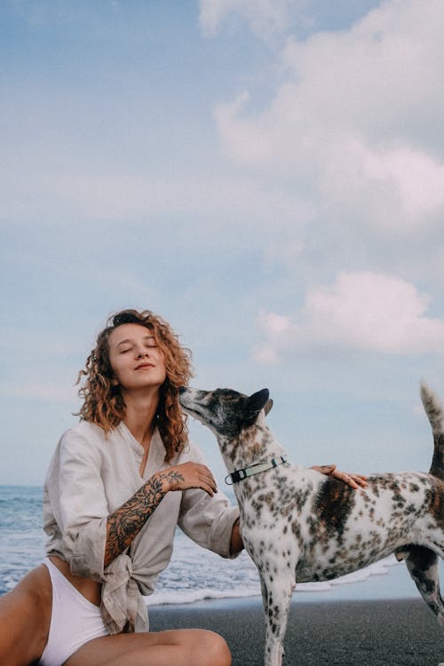 Woman in Linen Shirt Sitting on Beach Petting Dog