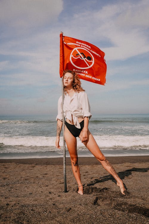 Woman Standing Next to Warning Sign on the Beach 