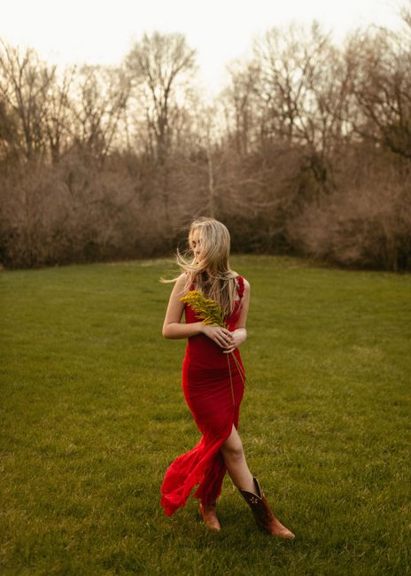Blonde woman in a flowing red dress walking on grass in Des Moines park during spring.