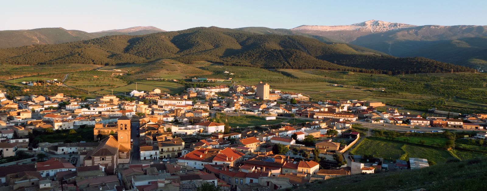 A breathtaking aerial view of a serene village nestled in lush mountains under a clear sky at sunset.