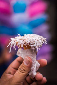 A hand holds a coconut-topped ice cream cone with a colorful blurred background.