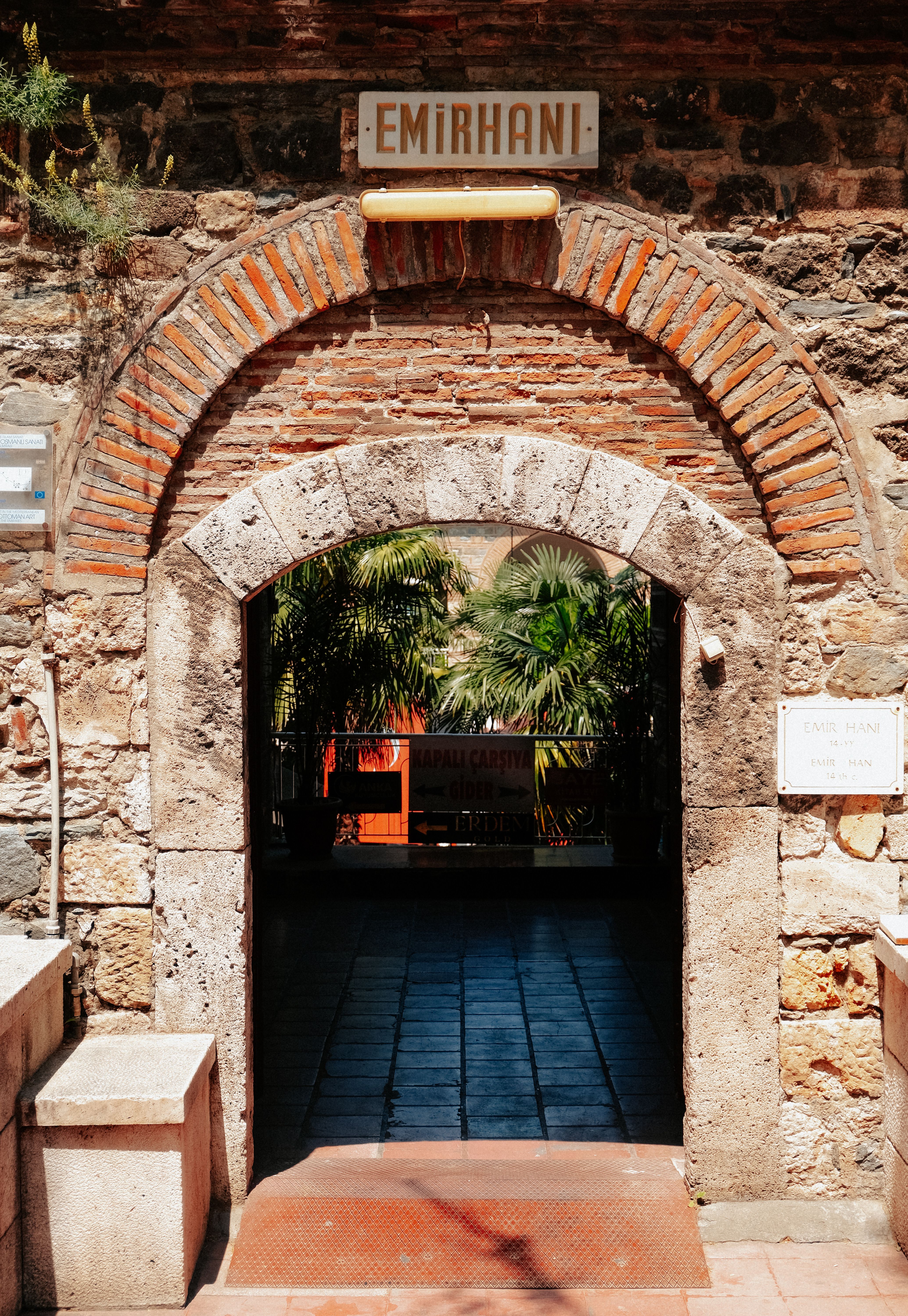 Stone entrance with palm trees and rustic bricks in Emirhan, showcasing historical architecture.