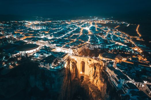 A breathtaking aerial view of Ronda, Spain at night featuring the illuminated Puente Nuevo.