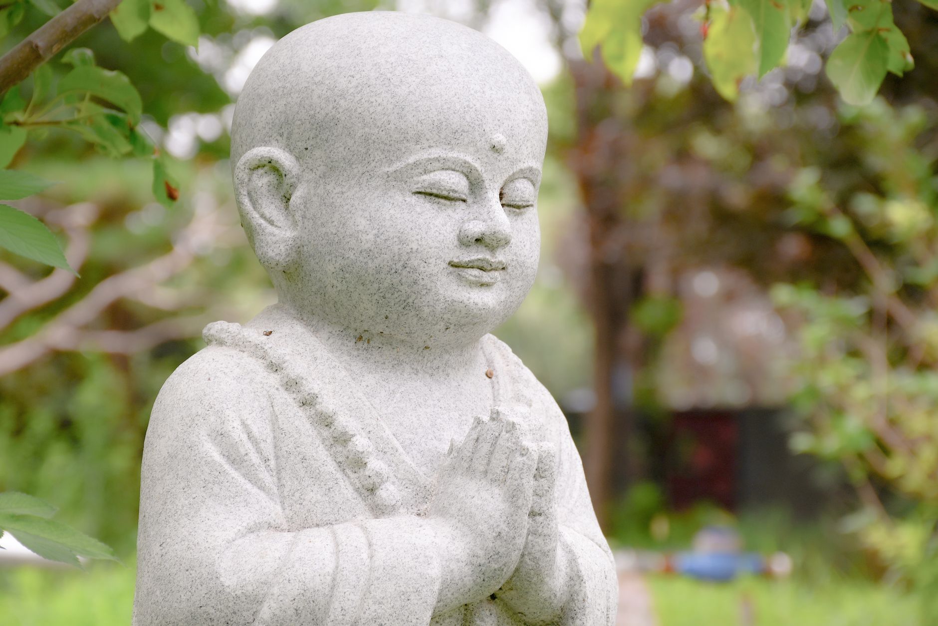 Peaceful stone sculpture of a Buddha figure in a tranquil garden setting, perfect for spiritual and nature themes.