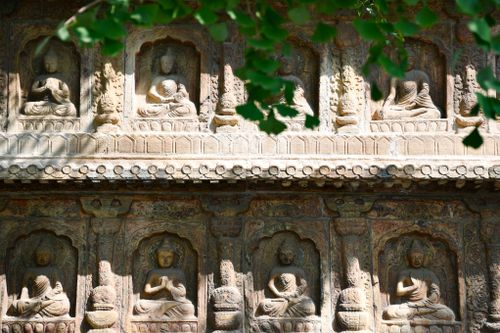 Free Detailed stone carvings of Buddha figures adorn an ancient temple facade, surrounded by nature. Stock Photo