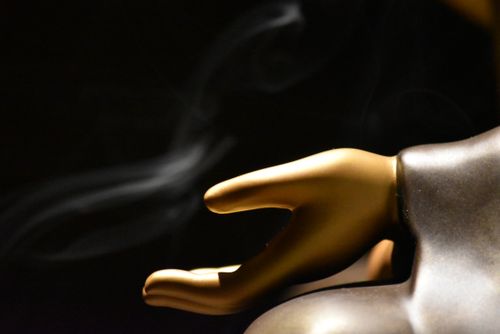Free Close-up of a golden sculpture hand against a dark background with smoke wisp. Stock Photo